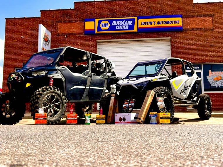 A black Can-Am and a Polaris RZR parked in front of the Justin's Automotive storefront